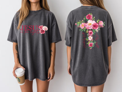 May include: Dark gray t-shirt with the text "JESUS is the Light" and a floral design. The back of the shirt features a cross adorned with pink roses and the words "Will be the Light".