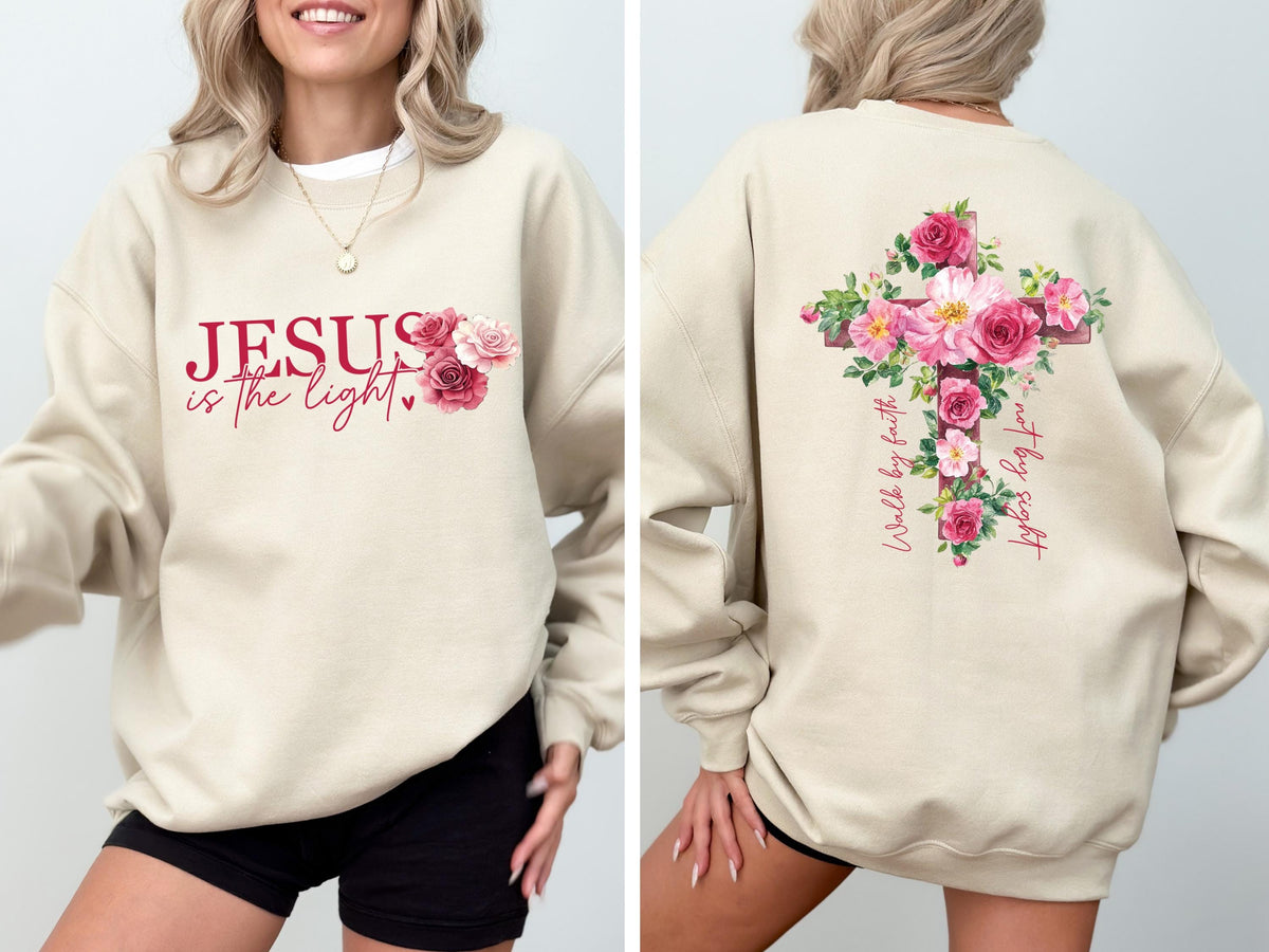 May include: Beige sweatshirt with the text "JESUS is the light" in burgundy script, accompanied by a floral arrangement of pink and red roses. The back features a cross design adorned with pink roses and the words "Walk by faith, not by sight."