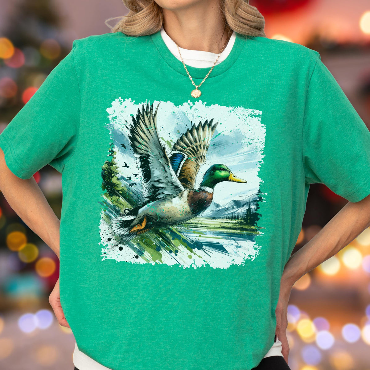 May include: A green t-shirt featuring a detailed graphic of a mallard duck in flight. The duck has green, blue, brown, and yellow feathers, with wings spread wide. The background includes a landscape with trees and mountains.