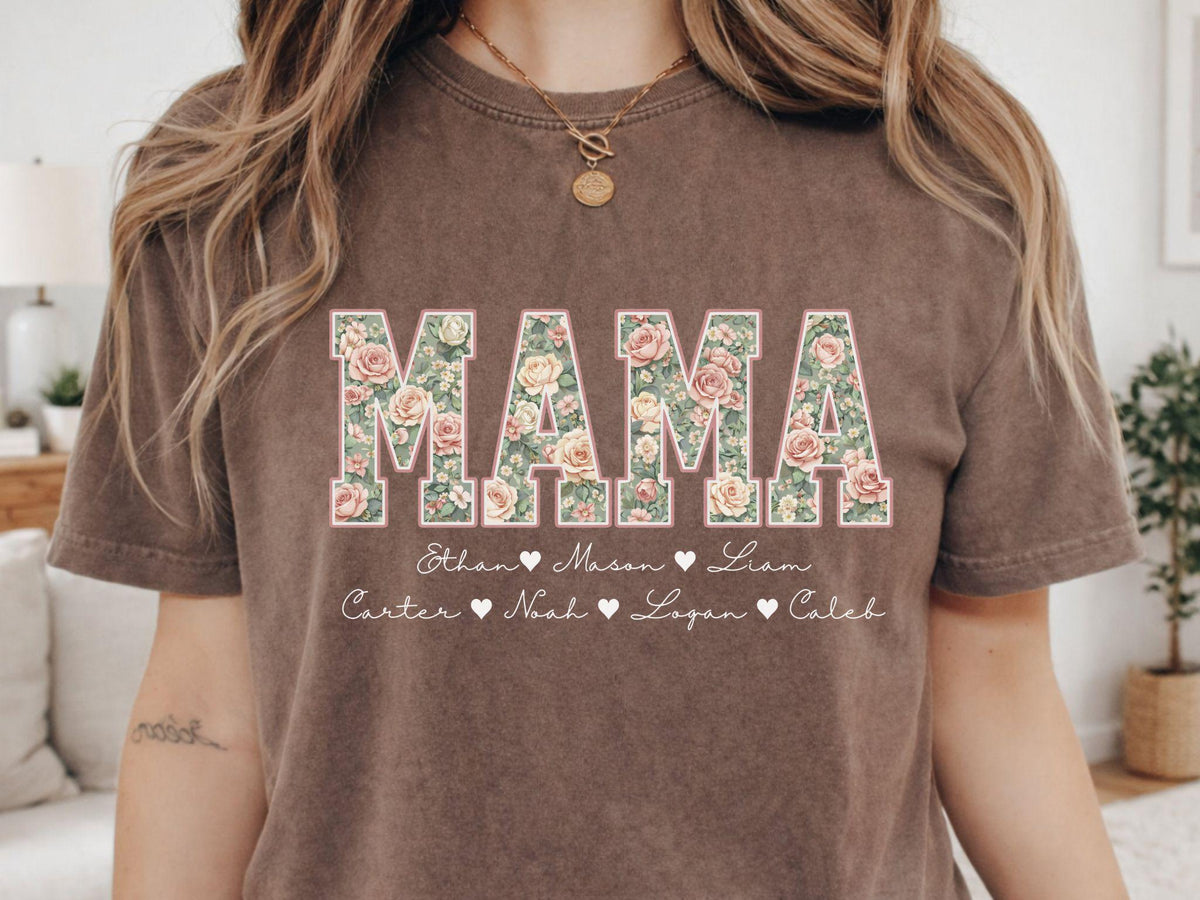 May include: Brown t-shirt with the word "MAMA" in large floral letters. Below the word "MAMA" are names with hearts. The shirt is a neutral color and has a vintage look.