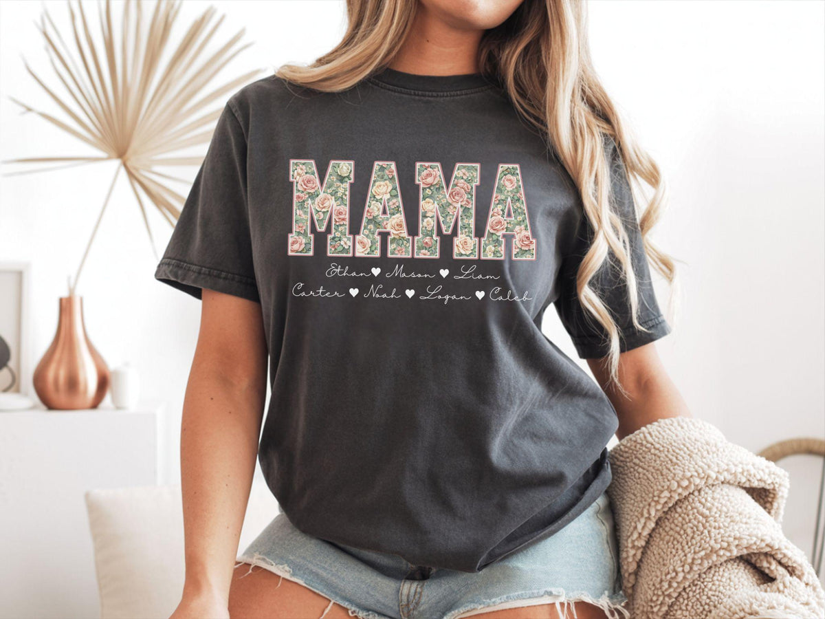 May include: Dark gray t-shirt with the word "MAMA" in a floral design. Below the word "MAMA" are the names Ethan, Mason, Liam, Carter, Noah, Logan, and Caleb. The shirt is a short-sleeved, crew neck style.