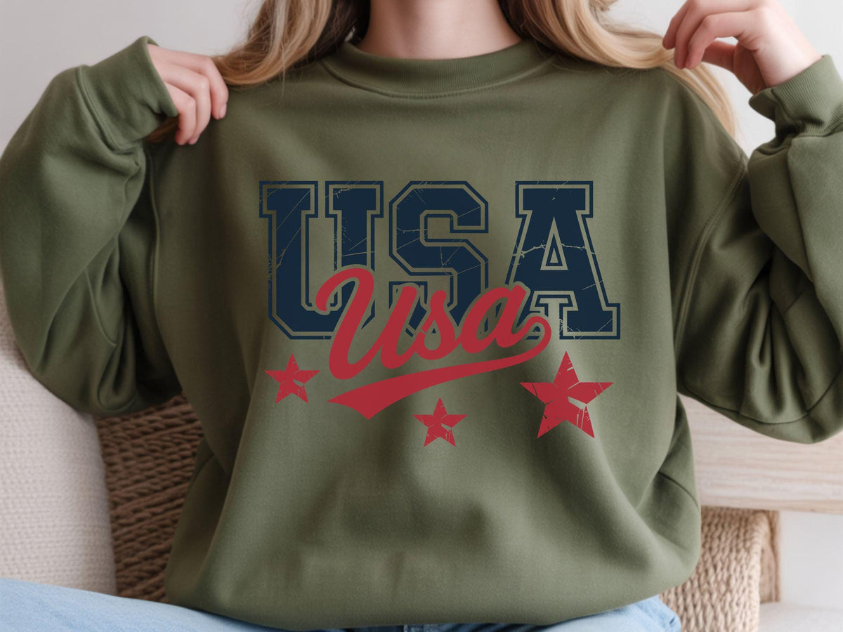 May include: Olive green sweatshirt with the word "USA" in navy blue block letters and red script. Three red stars are below the text. The sweatshirt is a casual style.