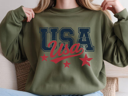 May include: Olive green sweatshirt with the word "USA" in navy blue block letters and red script. Three red stars are below the text. The sweatshirt is a casual style.