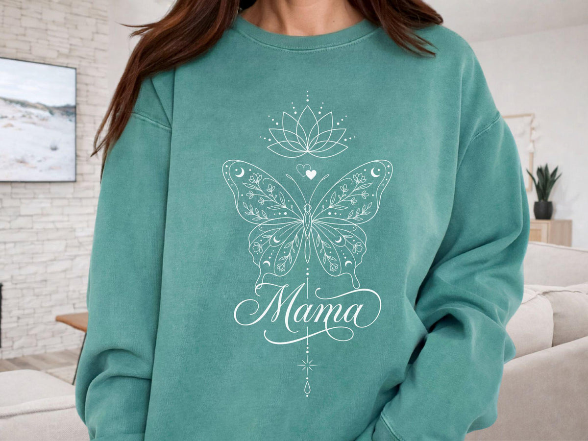 May include: Teal-colored sweatshirt featuring a white butterfly design with floral and moon details, a lotus flower, and the word "Mama" in cursive script. The sweatshirt has a relaxed fit and long sleeves, perfect for casual wear.