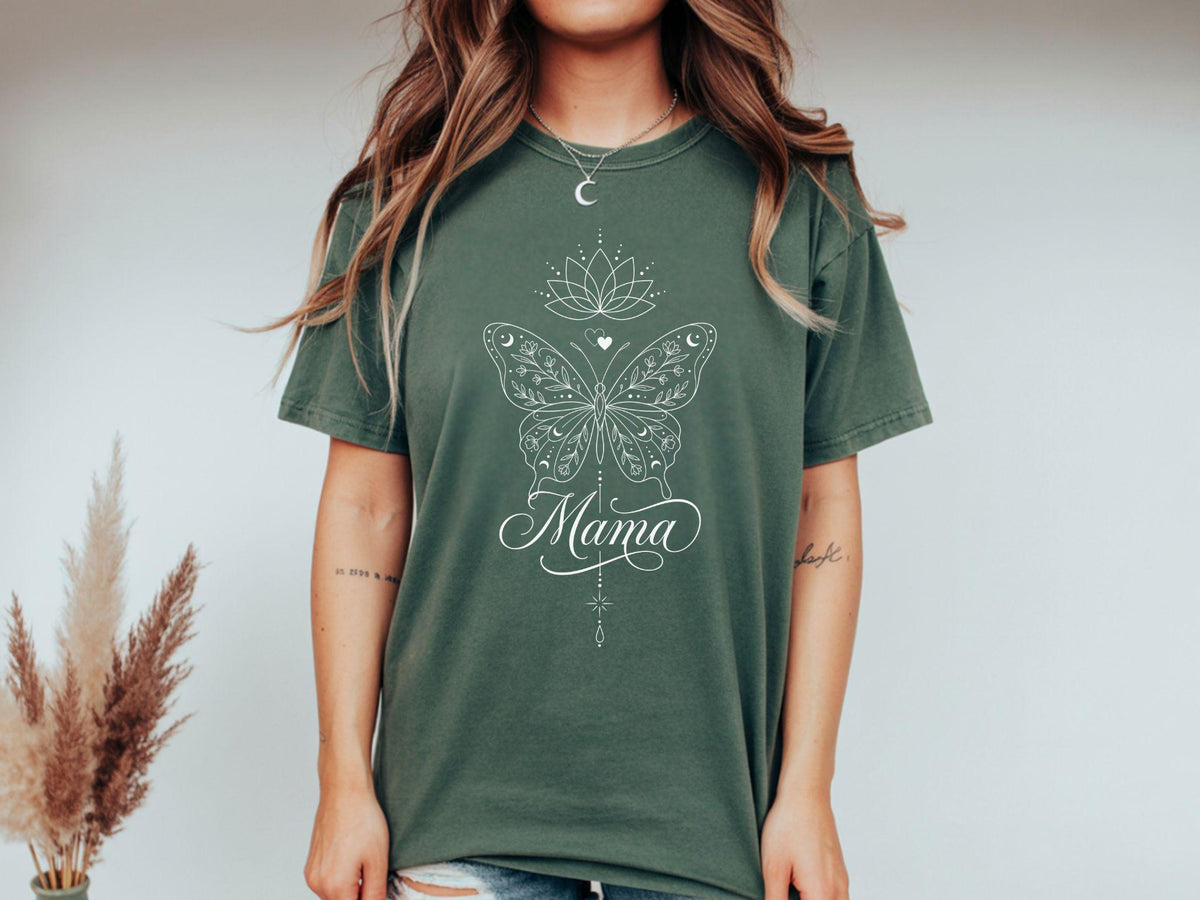 May include: An olive green t-shirt featuring a white butterfly design with the word "Mama" in script. The butterfly has intricate details, and the design includes a lotus flower and a crescent moon. The shirt is a relaxed fit.