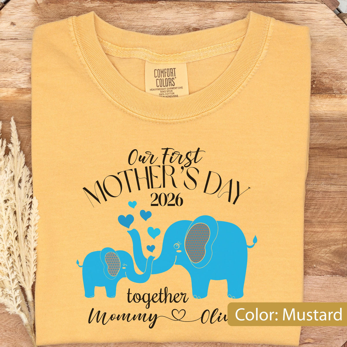 May include: Mustard-colored t-shirt with the text "Our First Mother's Day 2026" and a blue elephant design. The design includes two elephants with hearts and the words "together Mommy & Olivia".