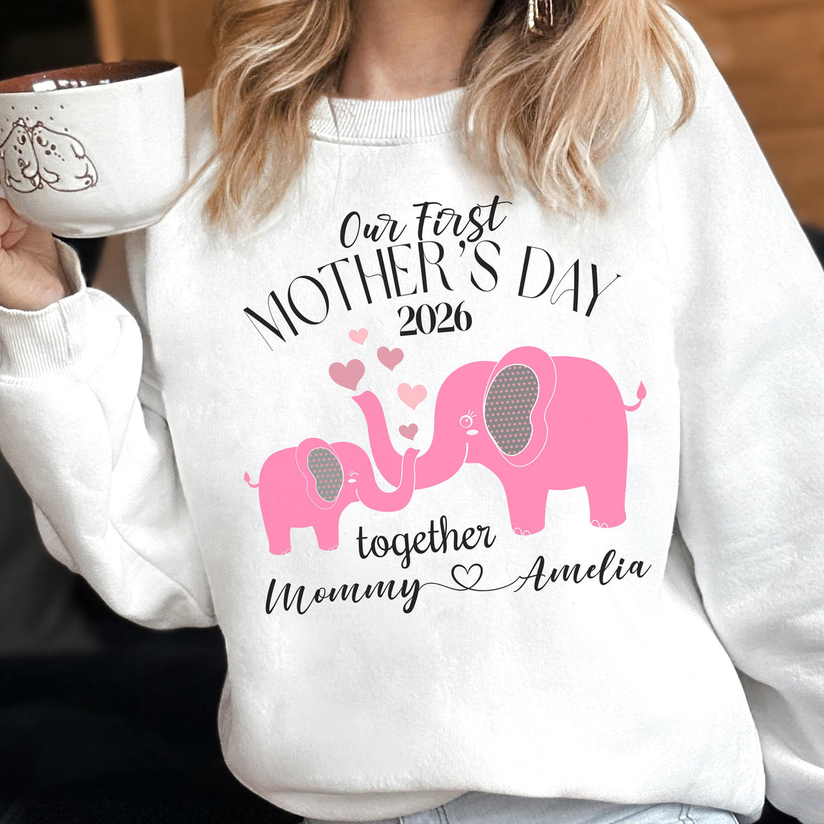 May include: White sweatshirt with the text "Our First Mother's Day 2026" and pink elephant graphics. The design includes hearts and the words "together Mommy Amelia". A heartwarming gift for Mother's Day.