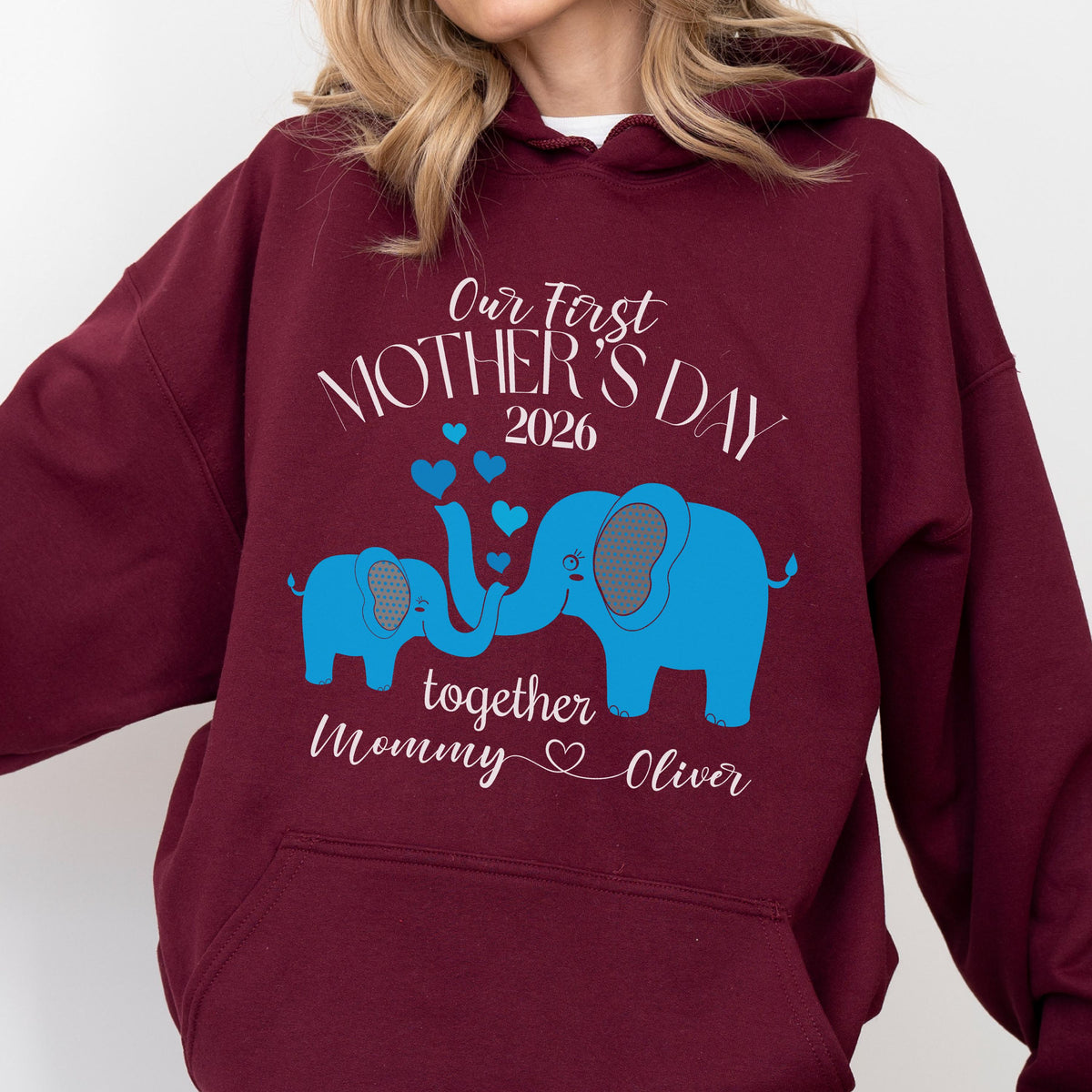 May include: Burgundy hoodie with a blue elephant design. The text reads "Our First Mother's Day 2026" with a smaller elephant and the words "together Mommy Oliver". The design includes blue hearts.