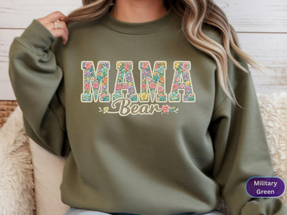 May include: Olive green sweatshirt with the text "MAMA Bear" in a floral design. The letters are filled with colorful flowers, and the word "Bear" is in a script font. The sweatshirt is a solid color.
