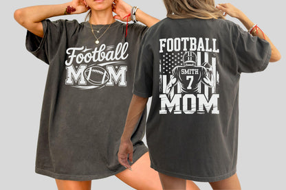 May include: Dark gray t-shirts with white text and graphics. One shirt says "Football MOM" with a football graphic. The other shirt has a football player graphic, the American flag, and the words "FOOTBALL MOM".