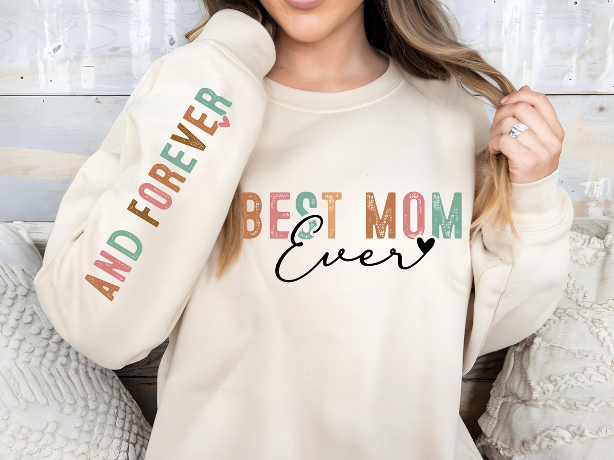 May include: Cream-colored sweatshirt with the text "BEST MOM Ever" in a mix of colors and a black heart. The sleeve reads "AND FOREVER" in a vertical design. A cozy and stylish apparel item.