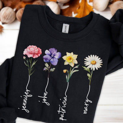 May include: Black sweatshirt featuring four colorful floral illustrations: a pink carnation, a purple pansy, a yellow daffodil, and a white daisy. Each flower has a name written below it in a cursive font: Jennifer, John, Patricia, and Mary.