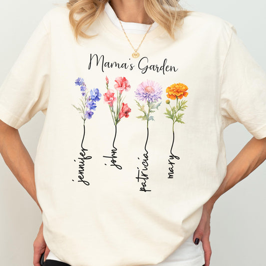 May include: Cream-colored t-shirt featuring the text "Mama's Garden" above four watercolor flowers. Each flower has a name written below it: Jennifer, John, Patricia, and Mary. The shirt is a casual, everyday wear item.