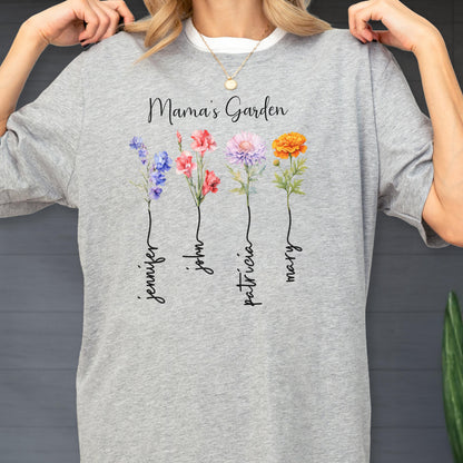 May include: A light gray t-shirt featuring the text "Mama's Garden" above four watercolor flowers. Each flower has a name written below it: Jennifer, John, Patricia, and Mary. The flowers are blue, pink, purple, and orange.