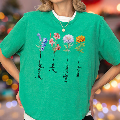 May include: A green t-shirt featuring four colorful floral illustrations with the names "Jennifer", "John", "Patricia", and "Mary" written below each flower. The shirt has a crew neck and short sleeves.