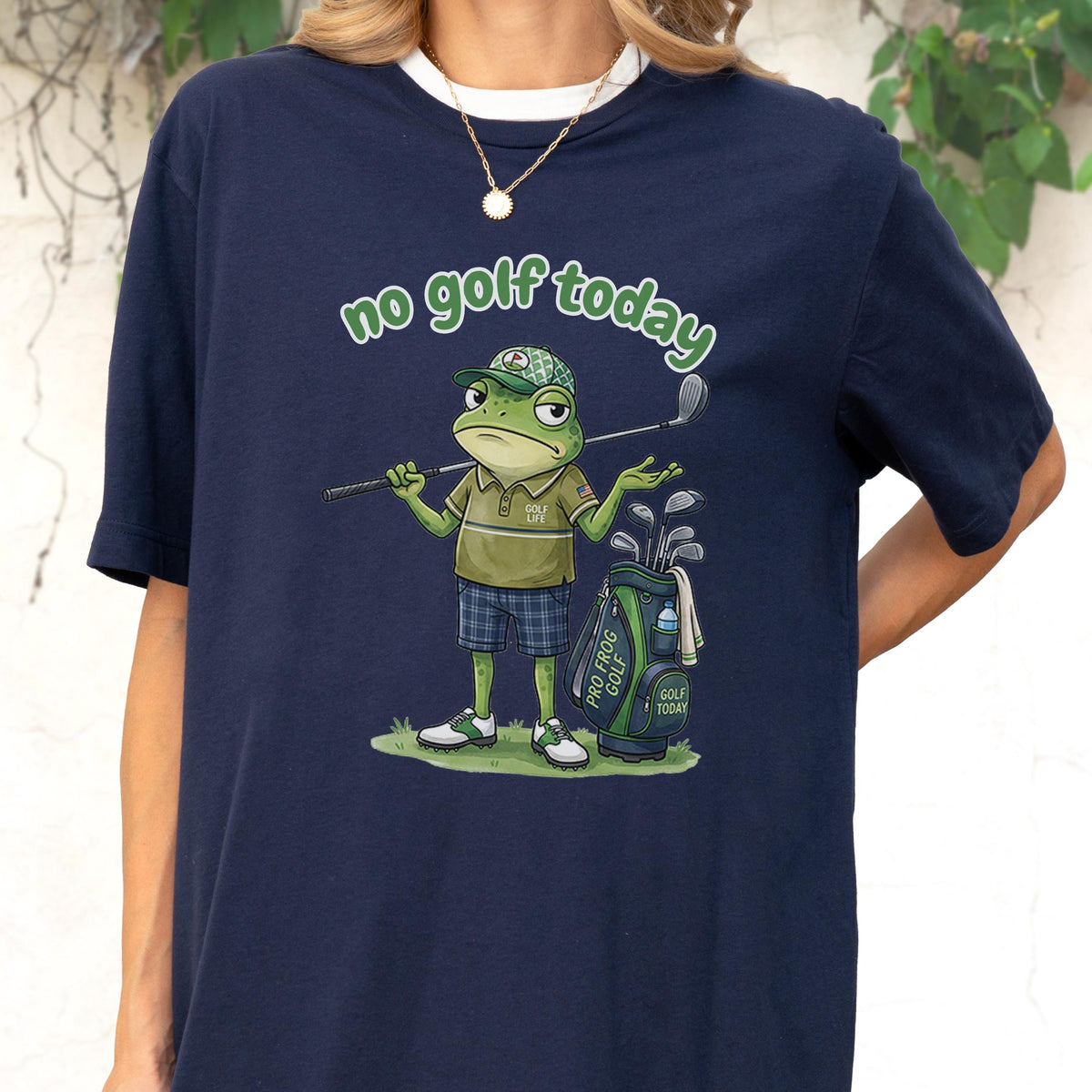 May include: Navy blue t-shirt with a graphic of a frog golfer holding a golf club and a golf bag. The text "no golf today" is arched above the frog. The frog is wearing a golf hat and shorts.