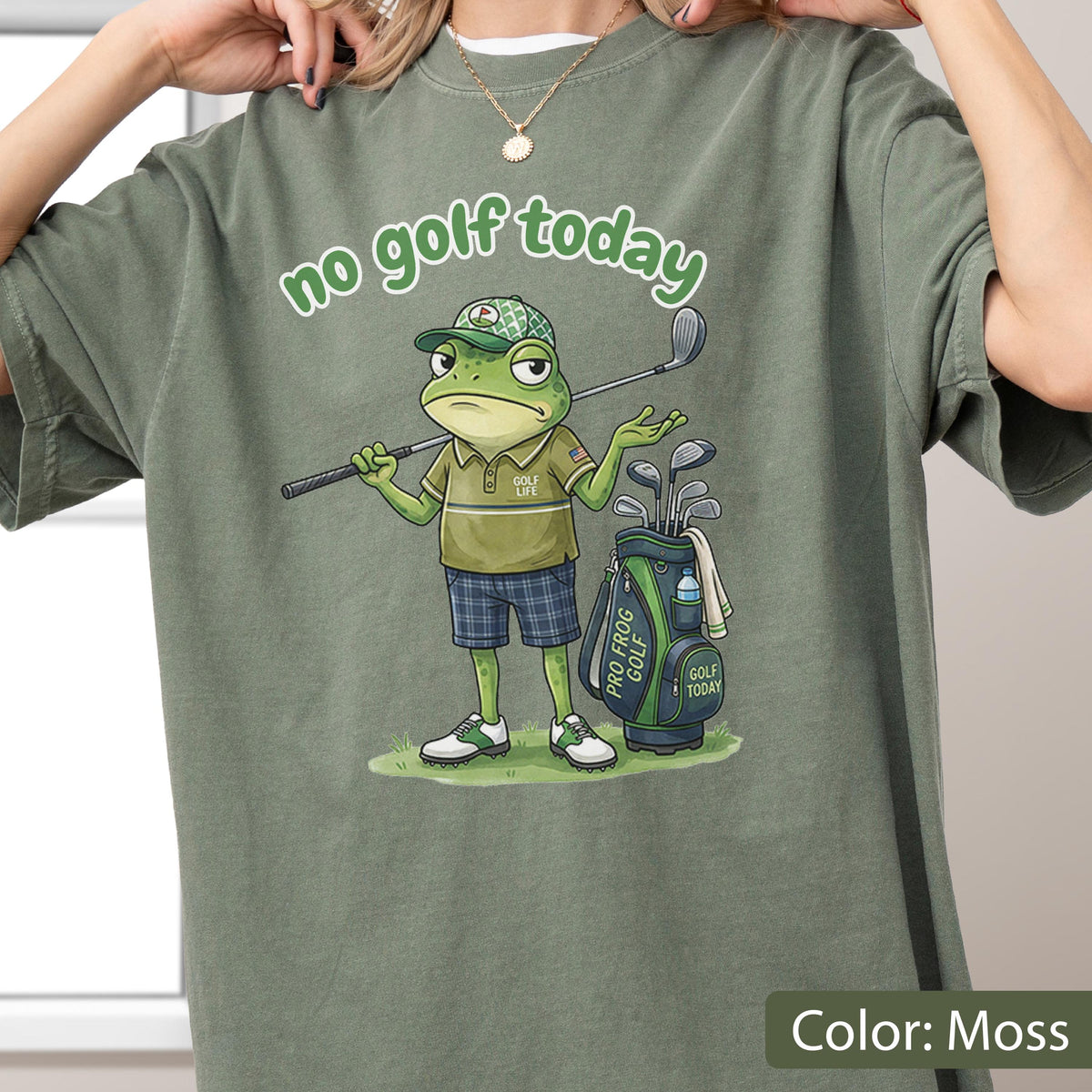 May include: Moss green t-shirt with the text "no golf today" above a cartoon frog golfer. The frog wears a golf hat, polo shirt, plaid shorts, and golf shoes. A golf bag and clubs are to the right.