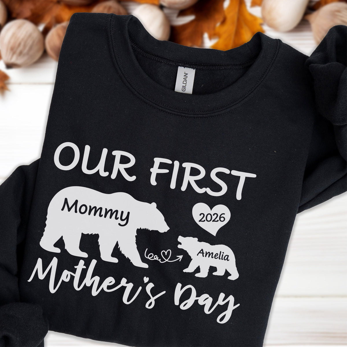 May include: Black sweatshirt with white text and graphics. The text reads "OUR FIRST Mommy Mother's Day" with a bear graphic and the name "Amelia" and the year "2026" inside a heart.