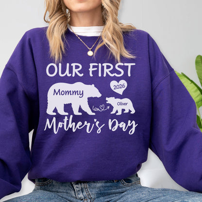 May include: A purple sweatshirt with white text and graphics. The text reads "OUR FIRST Mother's Day" with a bear graphic and the word "Mommy". A smaller bear graphic has the name "Oliver" and the year "2026" in a heart.