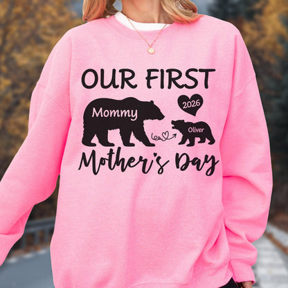 May include: Pink sweatshirt with the text "OUR FIRST Mother's Day" in black script. The design includes a bear graphic with the word "Mommy" and a smaller bear with the name "Oliver" and the year "2026".