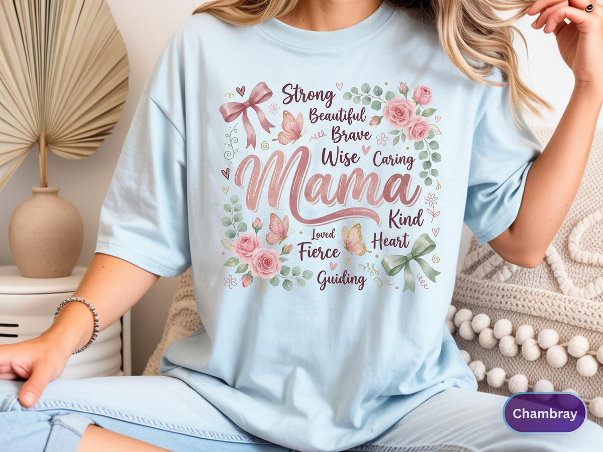 May include: Light blue t-shirt with the word "Mama" in a floral design. The design includes pink roses, butterflies, and the words "Strong, Beautiful, Brave, Wise, Caring, Kind, Heart, Loved, Fierce, Guiding". The shirt is a soft, comfortable material.