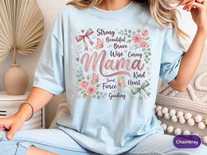 May include: Light blue t-shirt with the word "Mama" in a floral design. The design includes pink roses, butterflies, and the words "Strong, Beautiful, Brave, Wise, Caring, Kind, Heart, Loved, Fierce, Guiding". The shirt is a soft, comfortable material.
