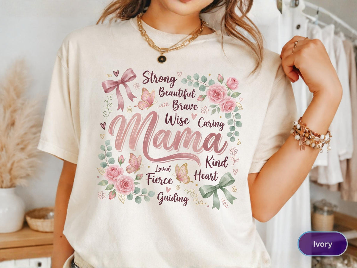 May include: Ivory-colored t-shirt with a floral and butterfly design. The design includes the word "Mama" in a script font, surrounded by words like "Strong," "Beautiful," and "Kind."