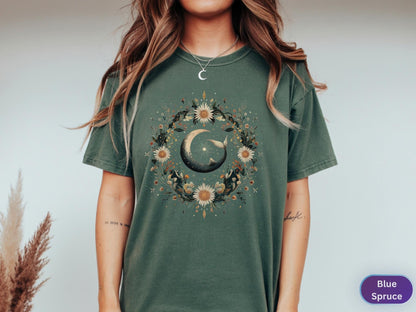 May include: A blue spruce t-shirt featuring a circular floral design with a crescent moon and a whale. The design includes sunflowers and other botanical elements. The shirt is a short-sleeved, crew neck style.