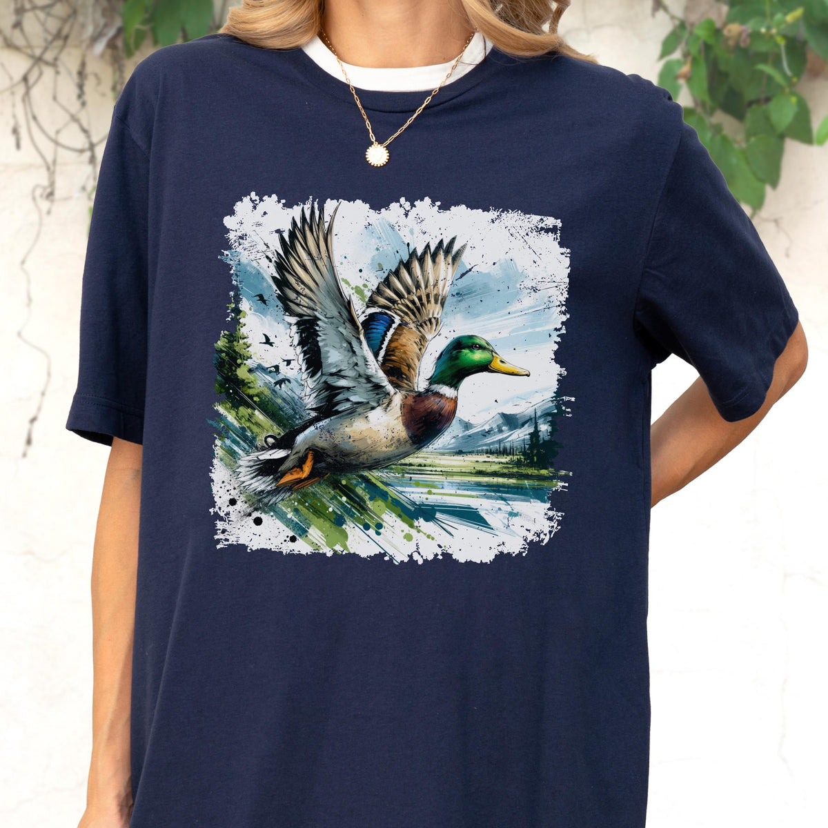 May include: Navy blue t-shirt featuring a detailed illustration of a mallard duck in flight. The duck has green, blue, and brown feathers, with wings spread wide. The artwork is set against a backdrop of a landscape with trees and mountains.