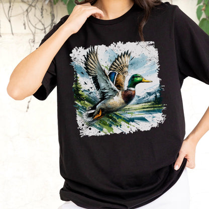 May include: Black t-shirt featuring a detailed graphic of a mallard duck in flight. The artwork showcases the duck with its wings spread, set against a backdrop of a landscape with trees, water, and mountains. The design has a distressed, painterly style.