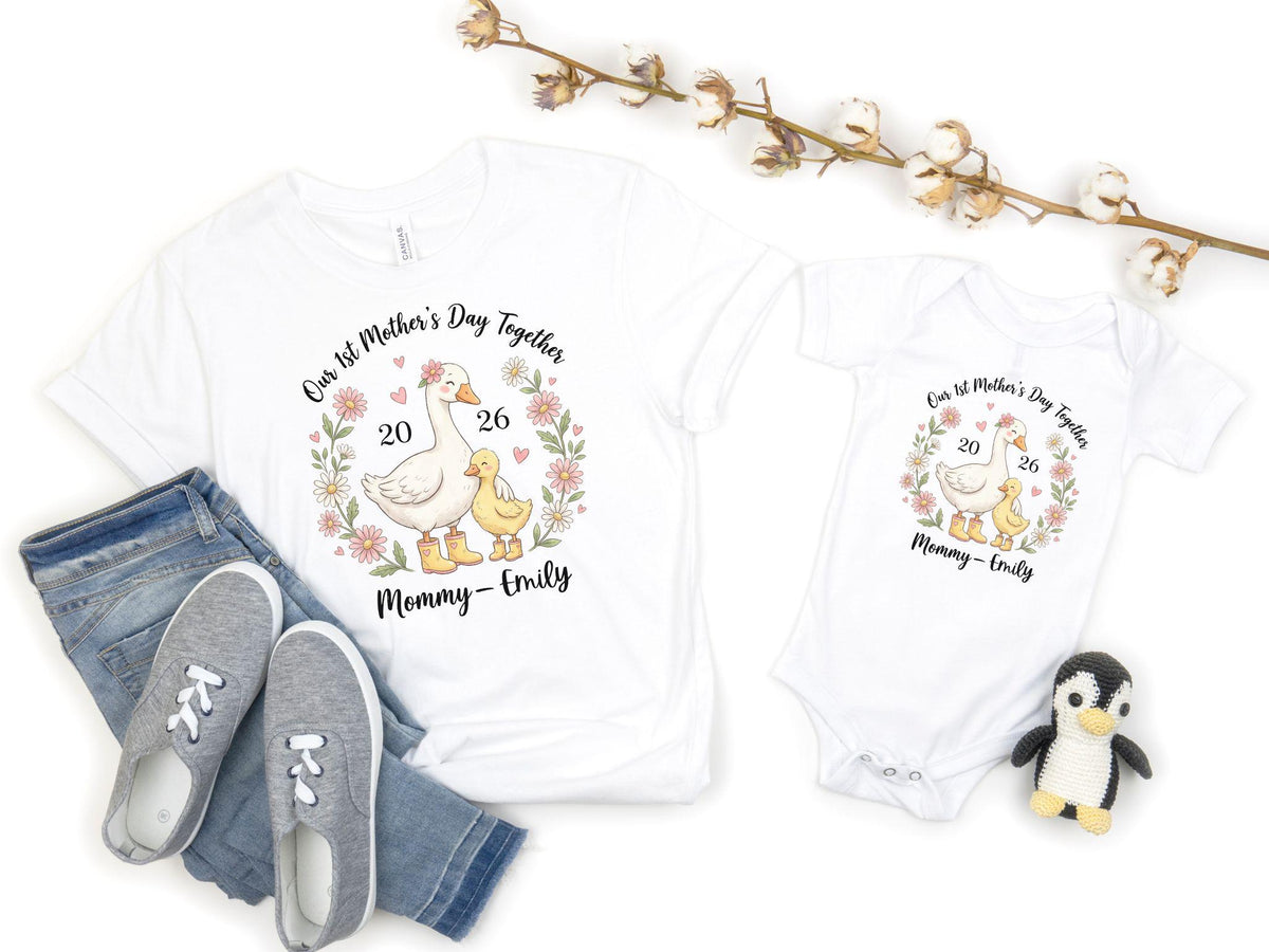 May include: White t-shirt and onesie set with a floral wreath design. The design includes a goose and a duckling, with the text "Our 1st Mother's Day Together" and "Mommy-Emily". The set is paired with blue jeans and gray sneakers.