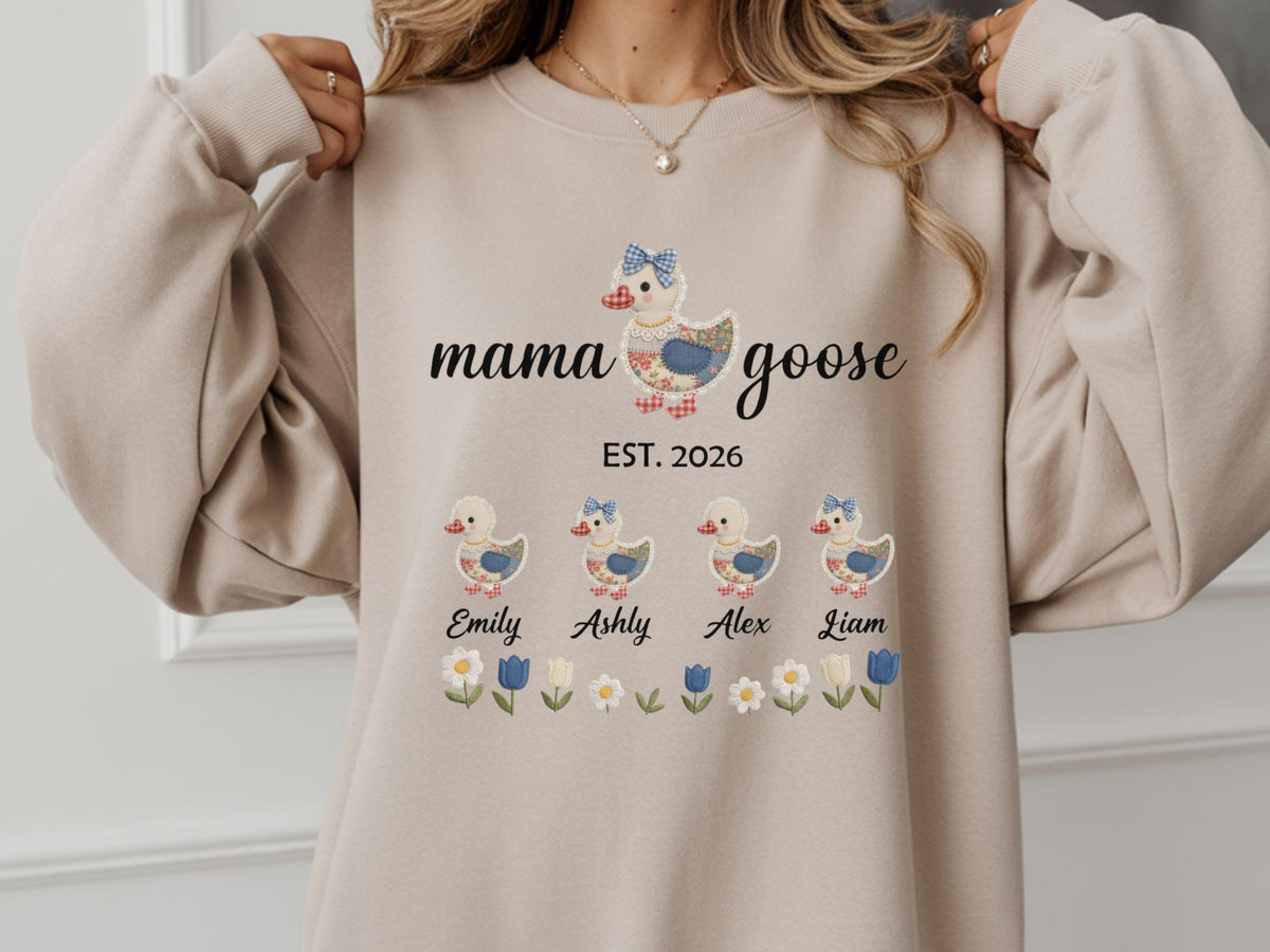 May include: Beige sweatshirt with a Mama Goose design. The design features a goose with a blue bow, the text "mama goose EST. 2026", and four ducklings with names. Floral and leaf accents are at the bottom.