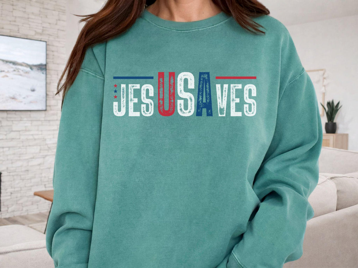 May include: Teal-colored sweatshirt with the text "JESUS SAVES" in white block letters. The letters "U" in "JESUS" and "S" in "SAVES" are red, and the letter "A" in "USA" is blue. The sweatshirt has a crew neck and long sleeves.