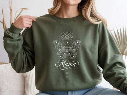 May include: Olive green sweatshirt with a white butterfly design, a lotus flower, and the word "Mama" in cursive script. The butterfly has intricate details and moon and star accents. A stylish and comfortable top.