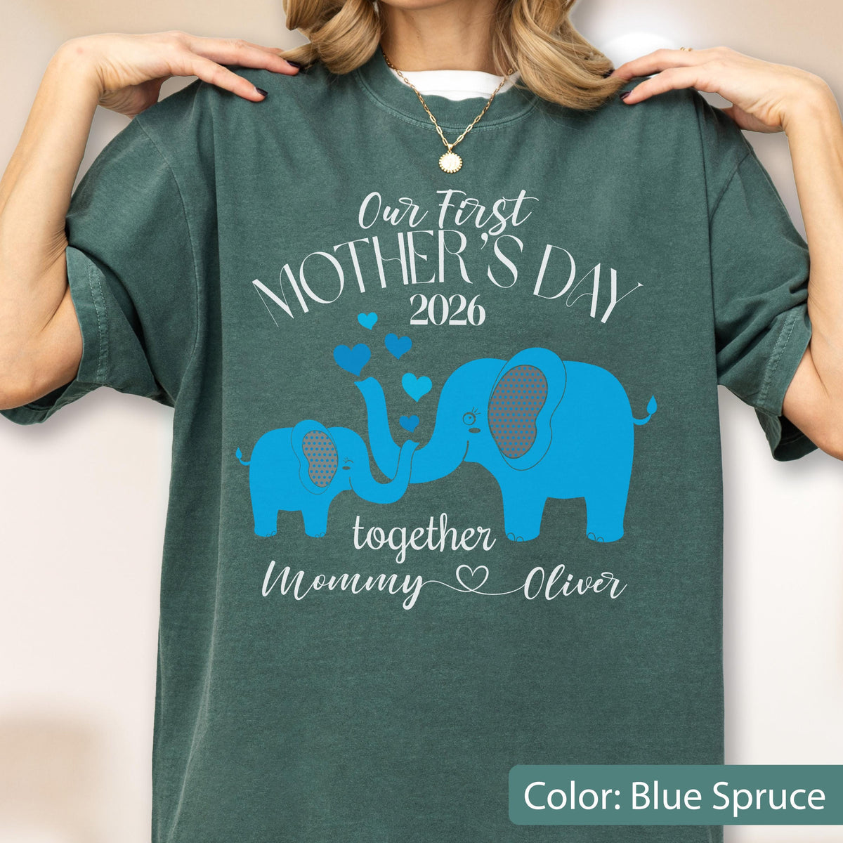 May include: Blue spruce t-shirt with the text "Our First Mother's Day 2026" and blue elephant graphics. The shirt also includes the words "together Mommy Oliver" in white script. The color is Blue Spruce.