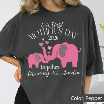 May include: Pepper-colored t-shirt with a pink elephant graphic. The design includes the text "Our First Mother's Day 2026" and "together Mommy Amelia" with heart accents. A heartwarming gift for Mother's Day.