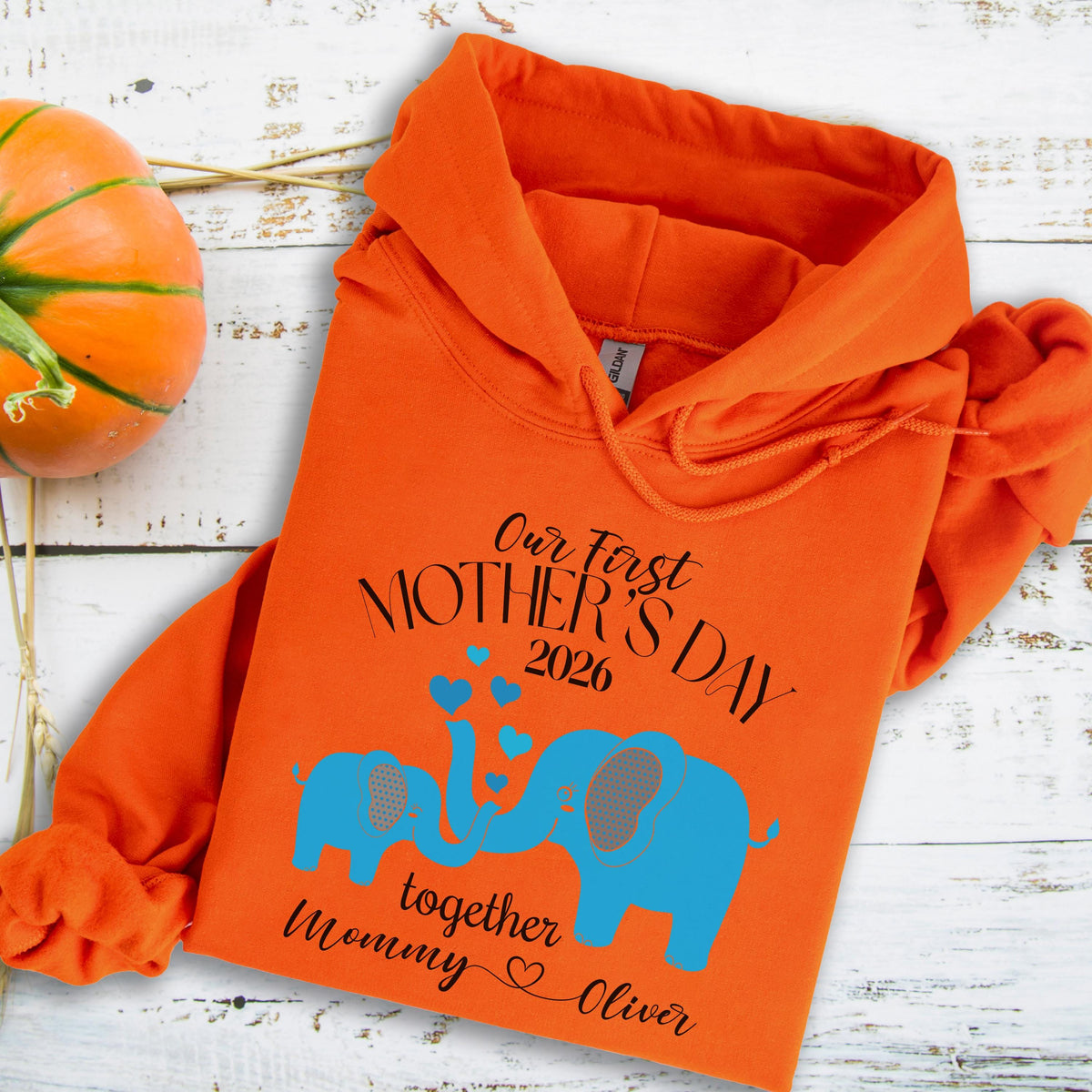 May include: An orange hoodie with the text "Our First Mother's Day 2026" and the words "together Mommy Oliver". The design includes two blue elephants with gray ears and hearts.