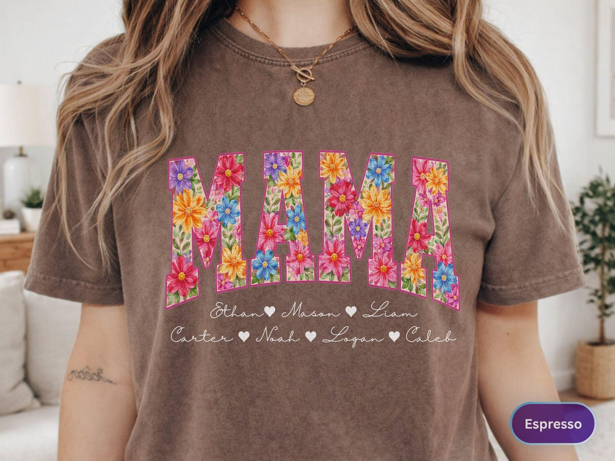 May include: Espresso-colored t-shirt with the word "MAMA" in large, floral-filled letters. Below the word are names with heart symbols. The shirt is a comfortable, casual style.