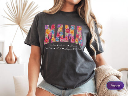 May include: Dark gray t-shirt with the word "MAMA" in colorful floral letters. Below the word "MAMA" are the names Ethan, Mason, Liam, Carter, Noah, Logan, and Caleb. The shirt is a casual style.