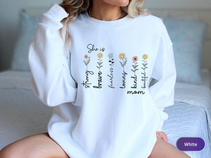 May include: White sweatshirt with the words "She is strong, brave, fearless, loving, kind, beautiful mom" in black script. The design includes floral accents in various colors. The sweatshirt is a crew neck style.