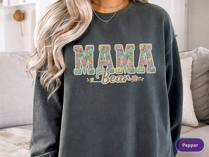 May include: Dark gray sweatshirt with the words "MAMA Bear" in a floral design. The letters are filled with colorful flowers, and the word "Bear" is in a script font. A casual and comfortable top.