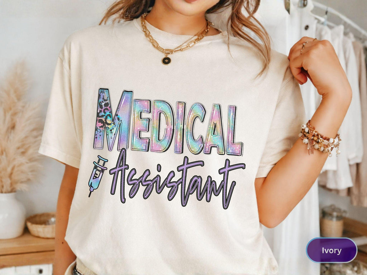 May include: Ivory-colored t-shirt with the words "MEDICAL Assistant" in a colorful, stylized font. The word "MEDICAL" has a leopard print design. A syringe graphic is next to the word "Assistant".