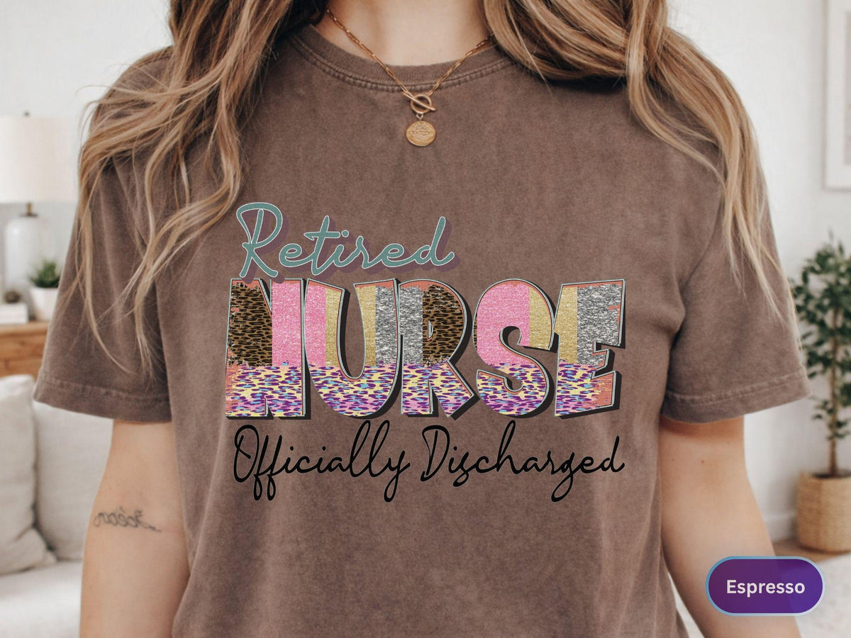 May include: Espresso-colored t-shirt with the words "Retired Nurse Officially Discharged" in a colorful, decorative font. The word "Nurse" has a leopard print design. The shirt is a casual style.
