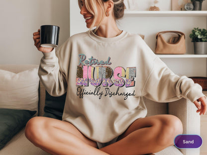 May include: Sand-colored sweatshirt with the words "Retired Nurse Officially Discharged" in a colorful, glittery design. The sweatshirt is a crew neck style and is made of a soft material.