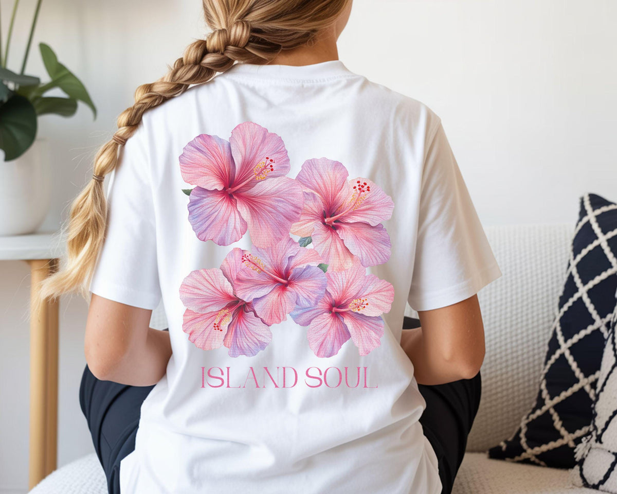 May include: White t-shirt featuring a cluster of pink and purple hibiscus flowers on the back. The words "ISLAND SOUL" are printed below the floral design. The shirt is a casual, everyday wear item.