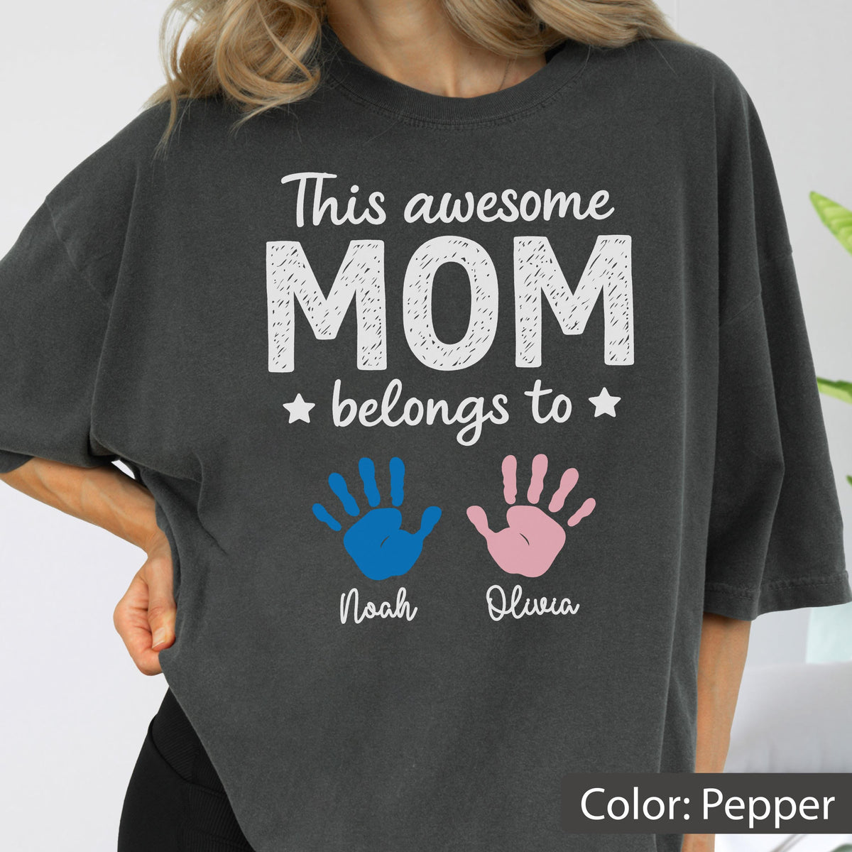 May include: Pepper-colored t-shirt with the text "This awesome MOM belongs to" and two handprints, one blue and one pink. Below the handprints are the names "Noah" and "Olivia".