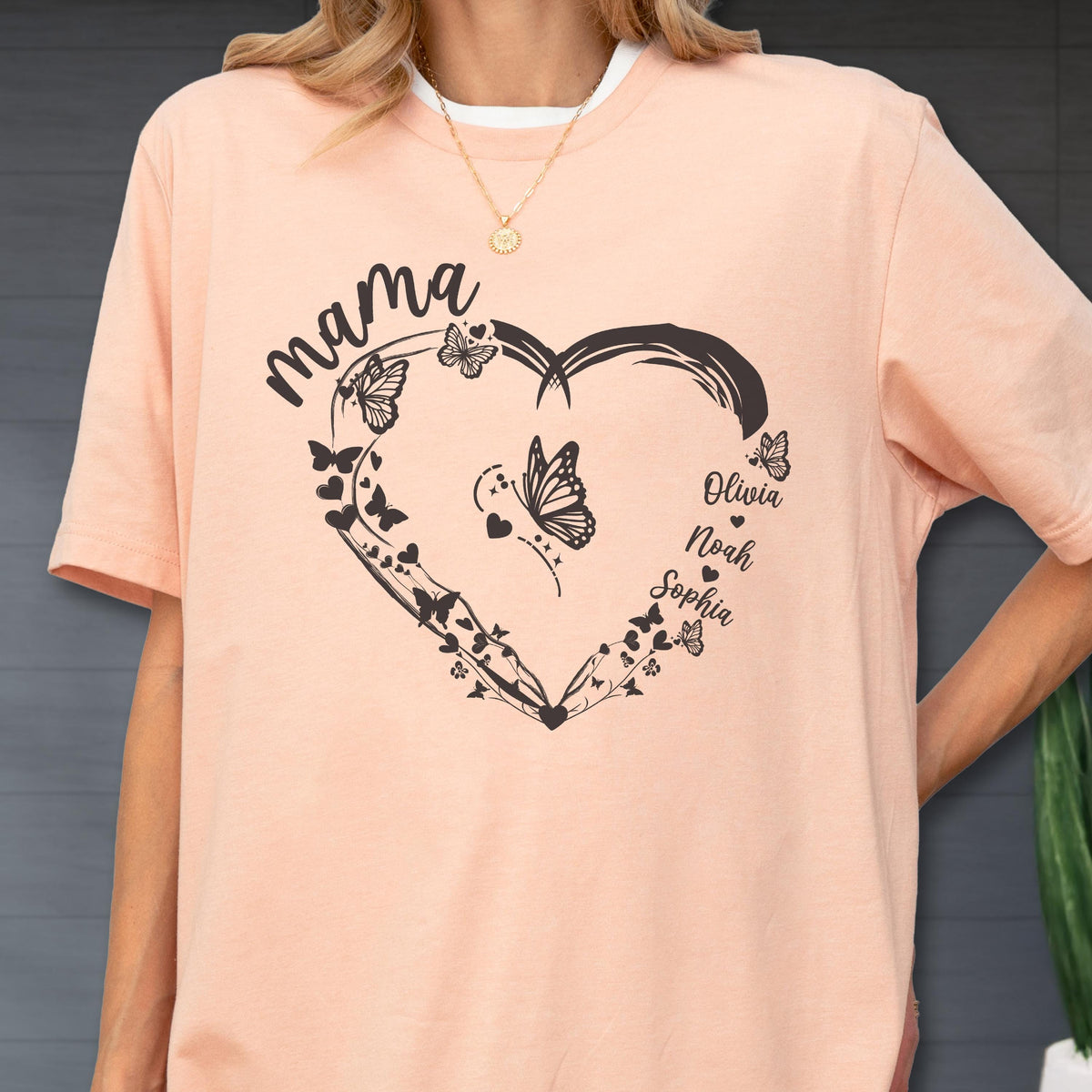 May include: A peach-colored t-shirt with a black heart-shaped design filled with butterflies and vines. The word "mama" is above the heart, and the names "Olivia, Noah, Sophia" are below.
