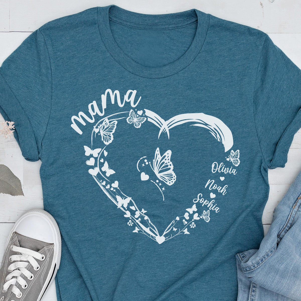 May include: Teal t-shirt with a white heart-shaped design. The heart is adorned with butterflies and the word "mama" at the top. Names "Olivia", "Noah", and "Sophia" are written inside the heart.