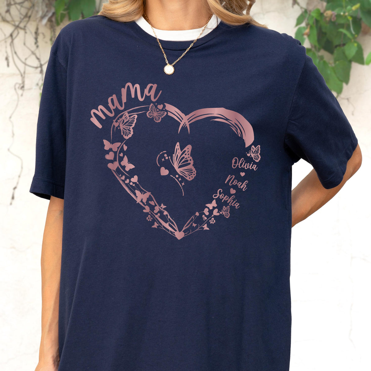 May include: Navy blue t-shirt with a white collar featuring a rose gold heart design filled with butterflies. The word "mama" is written above the heart, and the names "Olivia", "Noah", and "Sophia" are inside the heart.