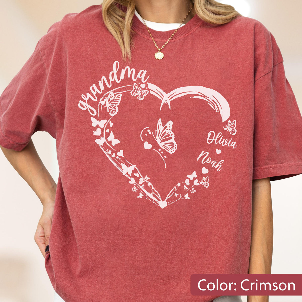 May include: Crimson-colored t-shirt featuring a white heart design with butterflies and the word "grandma". The names "Olivia" and "Noah" are also printed on the shirt. The shirt is a comfortable, casual style.